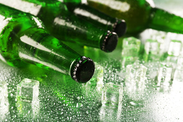 Glass bottles of beer with ice cubes on wet table background