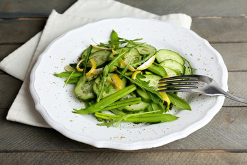 Green salad with cucumber, arugula and lemon peel on wooden table, closeup