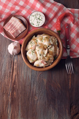 Fried dumplings with onion and bacon in frying pan, on wooden table background