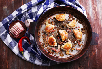Fried dumplings with onion and bacon in frying pan, on wooden table background