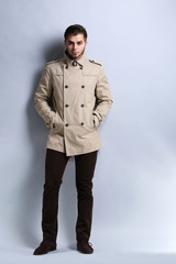 Young man in coat on gray background