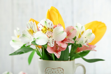 Beautiful flowers in cup, on wooden background