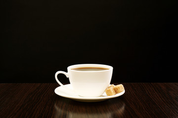 Cup of coffee with lump sugar on wooden table, on dark background