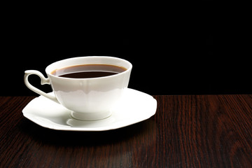 Cup of coffee on wooden table, on dark background