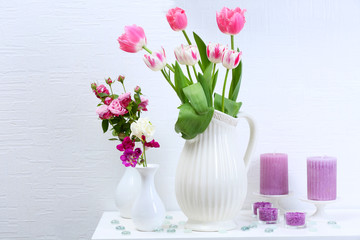 Beautiful composition with different flowers in vases on wall background