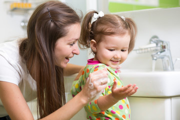 Smiling girl child and her mom washing hands and face with soap