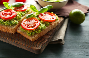 Vegan sandwich with avocado and vegetables on cutting board, on wooden background