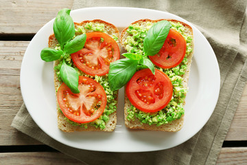 Vegan sandwich with avocado and vegetables on plate, on wooden background