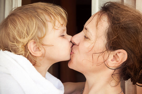 Happy mother kisses her cute baby girl in white towel