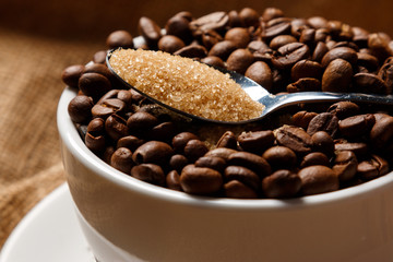 Cup filled with coffee beans and spoon with brown sugar