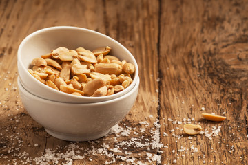 Roasted peanuts and salt in a bowl on a wooden background, selec