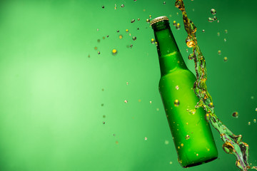Bottle of beer with splash, on green background