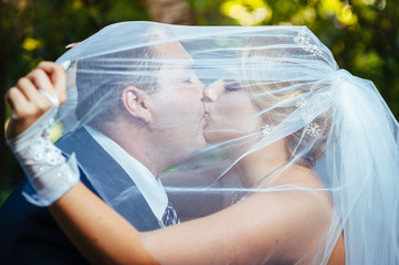 Bride And Groom Kissing Under Veil Holding Flower Bouquet In