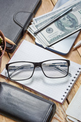 Workplace with notebook, phone, laptop, money, glasses.