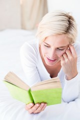 Smiling blonde woman lying on the bed and reading a book