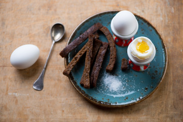 Breakfast soft-boiled eggs in eggcups with breadsticks and salt