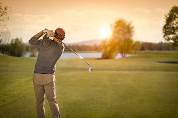 Male golf player swinging golf club at dusk. - obrazy, fototapety, plakaty