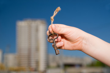 Child hand holding an old key to the house against the sky