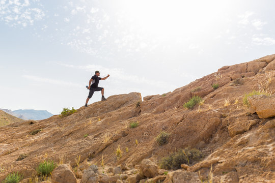 Spotsman running up stone desert hill.