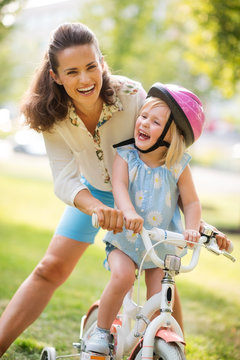 Laughing Mother And Daughter Learning How To Ride A Bike