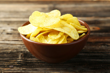 Potato chips in bowl on brown wooden background