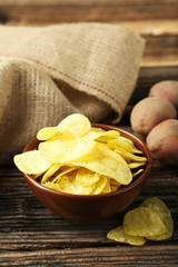Potato chips in bowl on brown wooden background