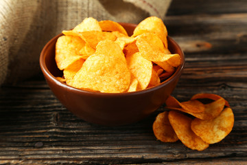 Potato chips in bowl on brown wooden background