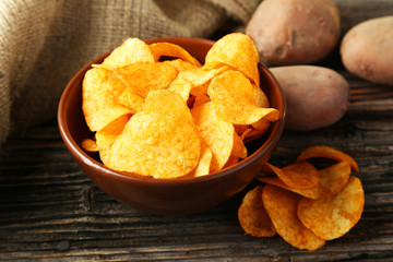 Potato chips in bowl on brown wooden background