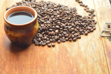 Roasted coffee beans are scattered near cup of coffee
