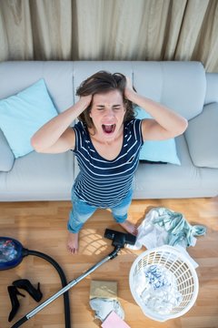 Angry woman in a chaotic living room with vacuum cleaner