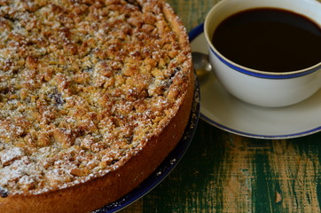 Plum crumble tart with cup of coffee on green background. 