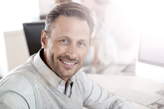 Cheerful man sitting in office and working on desktop