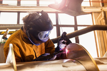 Young man with protective mask welding in a factory - obrazy, fototapety, plakaty