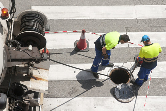 workers moves the manhole cover to check the sewer line