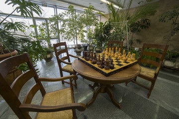 Chessboard on table with chairs in a hall with trees