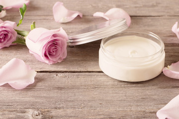 cosmetic cream with pink roses on old wooden table