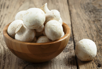 White mushrooms in a bowl on wooden table, selective focus