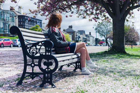 Woman sitting on park bench with cherry blossom