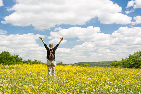 Junge Frau steht auf einer sommerlichen Blumenwiese und streckt die Arme in den Himmel