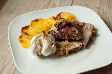 roasted pork with garlic and potatoes on white plate