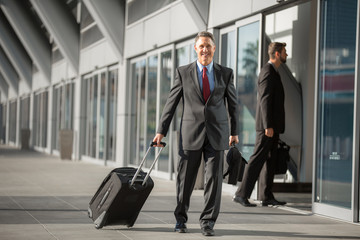 Executive man walks through airport after arriving on flight from business trip with luggage