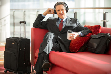 Older executive gentleman calmly sitting at the airport patient for flight listening to music on headphones