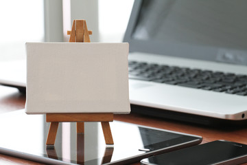 blank canvas and wooden easel on laptop computer as concept