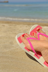 Womans feet with flip flops on the sand