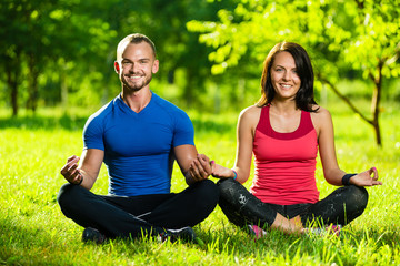 Young man and woman doing yoga in the sunny summer park