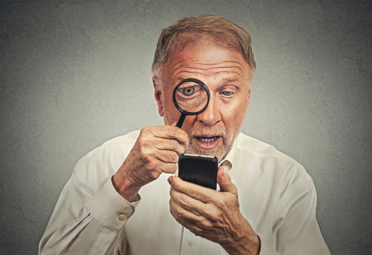Curious. Senior man looking through magnifying glass smartphone