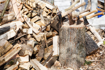 pile of firewoods and several axes in wooden block