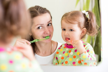 Woman teaching child daughter teeth brushing in bathroom. 
