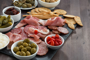 deli meat snacks, sausages and pickles on a dark wooden table