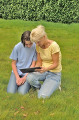 Naklejka na ściany i meble Family sitting on the lawn and using digital tablet